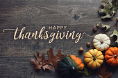 Happy Thanksgiving greeting text with fall pumpkins, squash and leaves over dark wood background