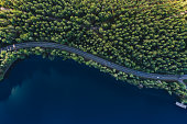 Aerial view of road with green woods by blue lakes water in Finland.