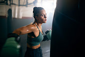 Young woman, with boxing gloves, punching the punching bag, while practicing kickbox in the gym