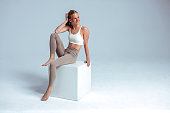 Smiling fitness model sitting on white cube in studio