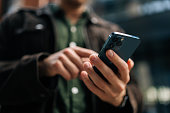 Close-up hands of unrecognizable man holding and using smartphone standing on city street, browsing internet, checking social media, using mobile application.
