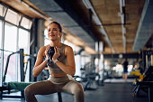 Happy female athlete doing squats while having weight training in a gym.