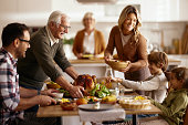 Happy senior man and his daughter serving Thanksgiving lunch to their family.