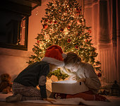 Children Opening Christmas Present by the Tree with Magical Light